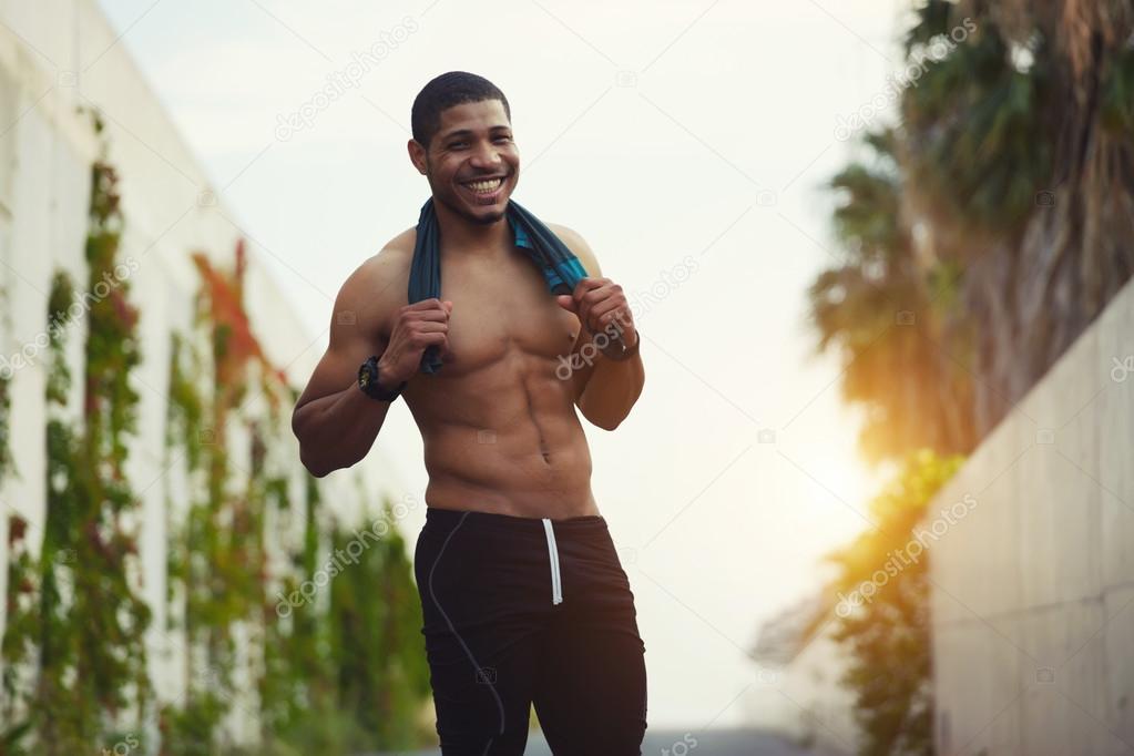 Handsome sportsman resting after running while holding shirt in the hands outdoors