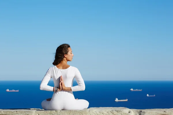 Йога на большой высоте с морем с кораблями на заднем плане, женщина сидит в позе йоги на удивительном морском фоне, женщина медитирует йогу наслаждаясь солнечным вечером, женщина делает йогу медитации на горном холме — стоковое фото