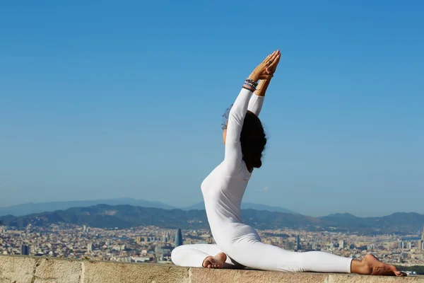Йога на большой высоте с большим городом на заднем плане, женщина растягивается в позе йоги на удивительном фоне города, женщина медитирует йогу и наслаждаясь солнечным вечером, женщина делает йогу на горном холме — стоковое фото