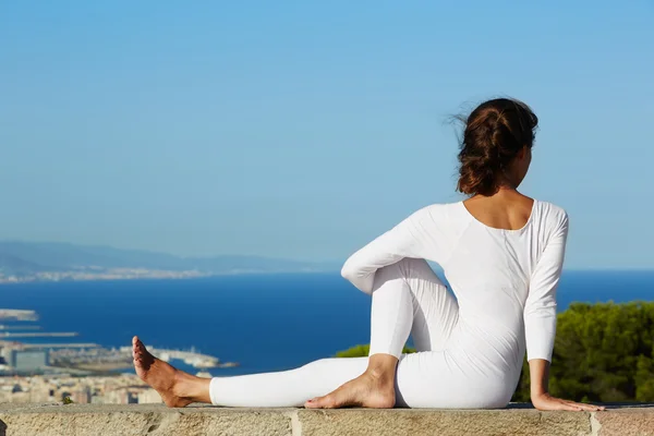 Yoga in großer Höhe mit Großstadt im Hintergrund, junge Frau sitzt in Yoga-Pose vor erstaunlicher Stadtkulisse, Frau meditiert Yoga und genießt sonnigen Abend, Frau macht Yoga auf Berg — Stockfoto