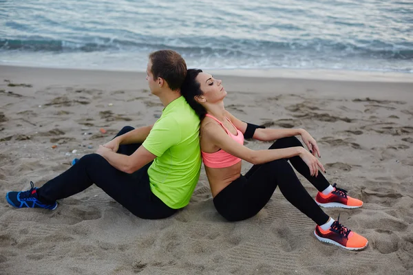 Sportpaar, das nach dem Training ausgeruht am Strand entlangläuft, sexy fitte Frau und Mann in fluoreszierendem Hemd, die nach dem Lauf Pause machen, ein paar Läufer, die sich nach dem Fitnesstraining im Freien ausruhen — Stockfoto