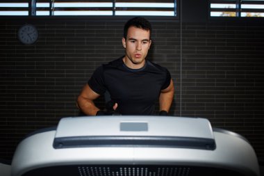 Fit man running in a gym on a treadmill looking to the screen, attractive sportsman at the gym doing exercise on the treadmill, handsome brunette man at workout in gym running fast on a treadmill