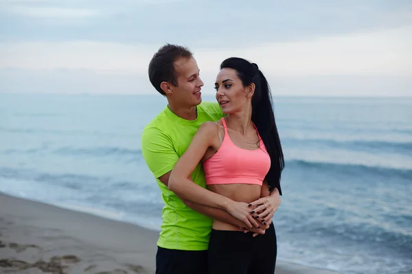 Happy smiling couple in love, cheerful couple of young man and woman embracing each to other, romantic couple standing on the beach enjoying beautiful evening, young happy people living good — Stock fotografie