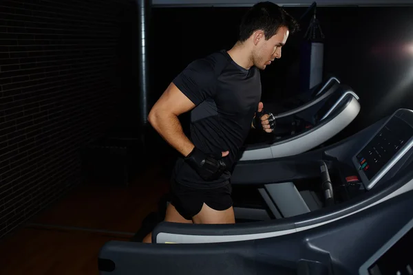 Deportista guapo en el gimnasio haciendo ejercicio en la cinta de correr, hombre corriendo en un gimnasio en una cinta de correr mirando a la pantalla, joven atractivo entrenando en interiores — Foto de Stock