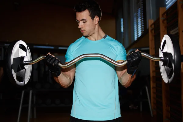 Homem atlético bombeando músculos com haltere, jovem atraente treinando interior, homem fazendo exercício pesado haltere para bíceps, musculoso musculoso fazendo exercícios com haltere no ginásio — Fotografia de Stock