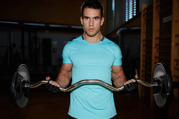 Atletisk mand pumpe op muskler med håndvægt, attraktiv ung mand træning indendørs, mand gør tunge håndvægt motion for biceps, bodybuilder mand laver øvelser med håndvægt i gymnastiksalen - Stock-foto