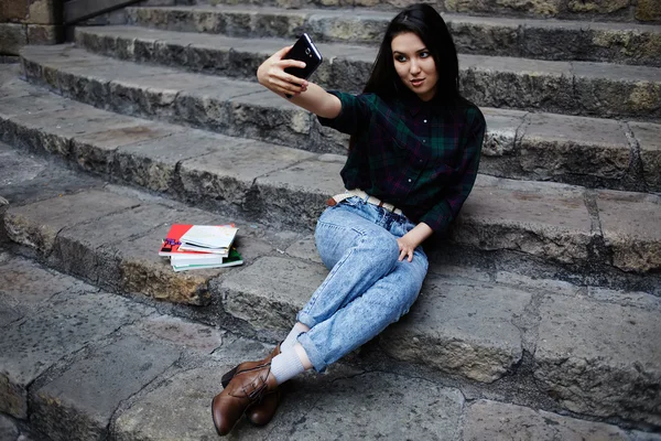 Rindo menina estudante tomando um auto-retrato com telefone inteligente sentado em passos, linda garota hipster fotografar-se com telefone celular, menina encantadora sorrindo ao tomar um self-ie ao ar livre — Fotografia de Stock