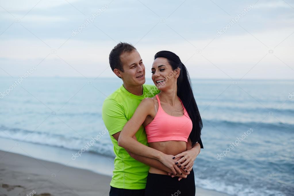 Cheerful couple in love embracing each to other standing on the beach, romantic couple  enjoying spending time together at beautiful evening, sporty couple of male and female runner