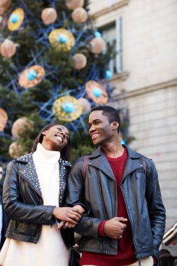 Laughing couple on christmas vacation walking in the city, beautiful young couple having fun walking on vacation holidays, romantic couple walk on christmas tree background on big square