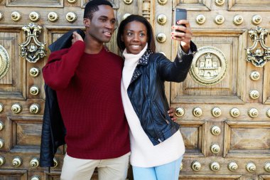 Laughing couple on christmas vacation making self portrait with digital camera on phone, tourist man and woman taking self-portrait picture with smart-phone, outdoors portrait of smiling couple clipart