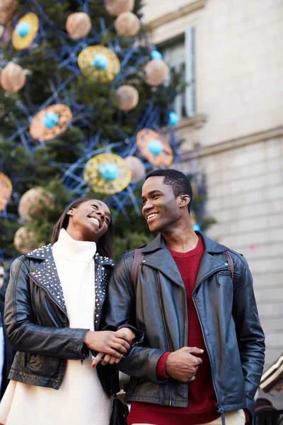 Pareja sonriente en vacaciones de Navidad caminando en la ciudad, hermosa pareja joven divirtiéndose caminando en vacaciones, pareja romántica caminando en el fondo del árbol de Navidad en la plaza grande — Foto de Stock