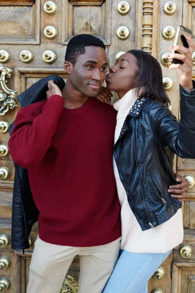 Jovem mulher beijando seu namorado na bochecha tirando foto auto-retrato com telefone inteligente — Fotografia de Stock