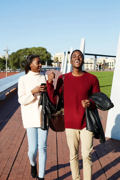 Longitud completa de estudiantes universitarios alegres caminando en el campus, jóvenes estudiantes con estilo caminando durante el descanso, amigos pasándola bien juntos, dos amigos universitarios riendo pasándola bien — Foto de Stock