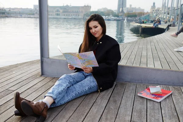 Encantadora menina asiática sentada com mapa da cidade aberto no cais de madeira, atraente menina turística descansando depois de andar sentado no cais de madeira no porto marítimo, bela menina estudante segurando mapa da cidade em mãos sorrindo — Fotografia de Stock