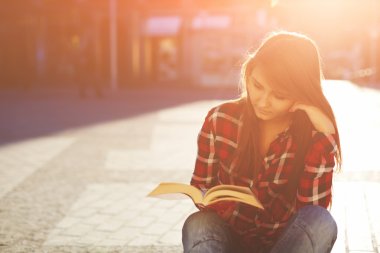 hipster woman enjoying a good book sitting at sunny evening outdoors