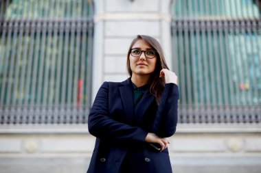 Beautiful girl in a long blue coat and glasses, waiting for her boyfriend at the entrance to the park