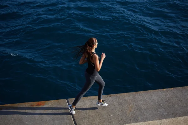 Imagem dinâmica com menina esporte em ação correndo sobre fundo ondas do oceano — Fotografia de Stock