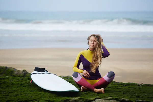 Una chica en un vestido brillante para montar una tabla de surf se sienta en la playa después de la ola conquistada — Foto de Stock