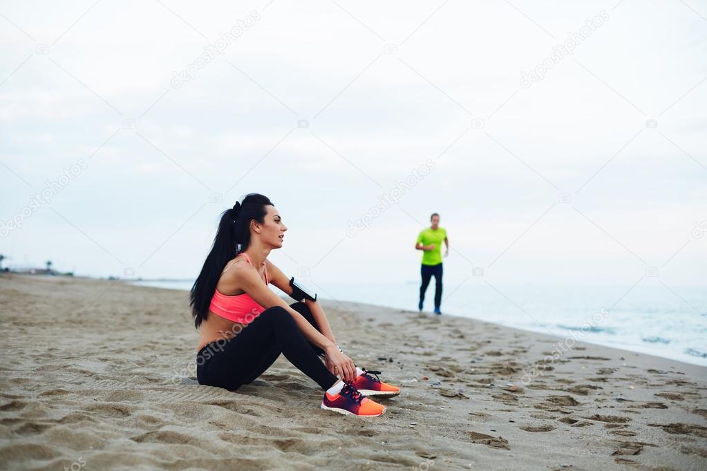 Man and woman together play sports until the guy running girl resting sitting on the sand