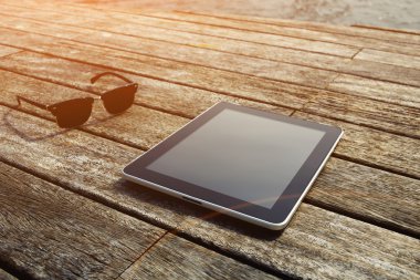 Sunglasses and digital tablet on wooden jetty