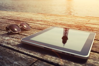 Sunglasses and digital tablet on wooden jetty