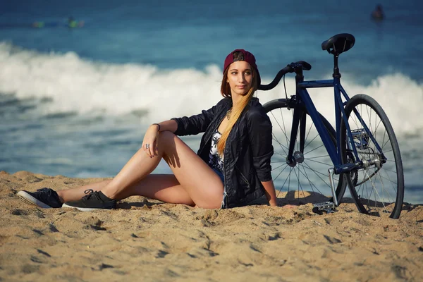 Jonge vrouw zitten op het zand met fiets — Stockfoto