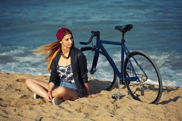 Ung kvinna sitter i sanden med cykel — Stockfoto