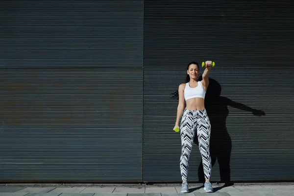 Woman lifting weights standing with arms tense — Stock Photo, Image