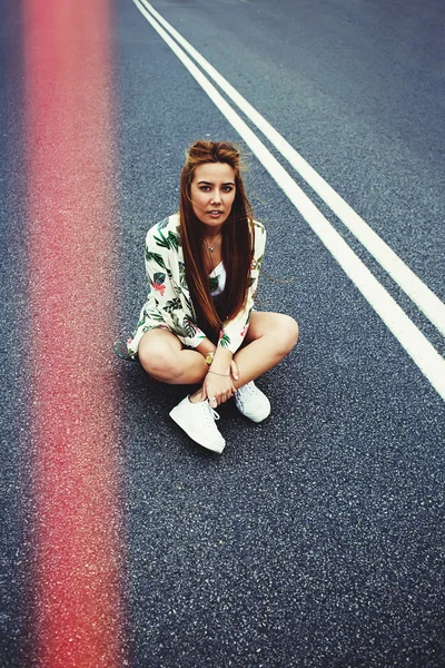 Hipster menina sentado no meio da estrada de asfalto — Fotografia de Stock