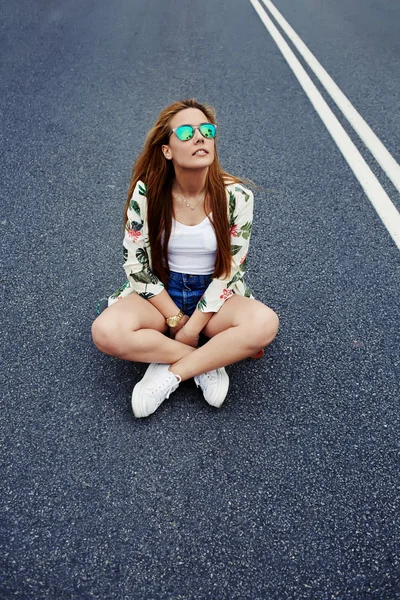 Hipster girl sitting  in the middle of asphalt road — Stock Photo, Image