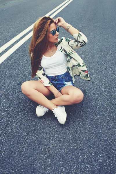 Hipster menina sentado no meio da estrada de asfalto — Fotografia de Stock