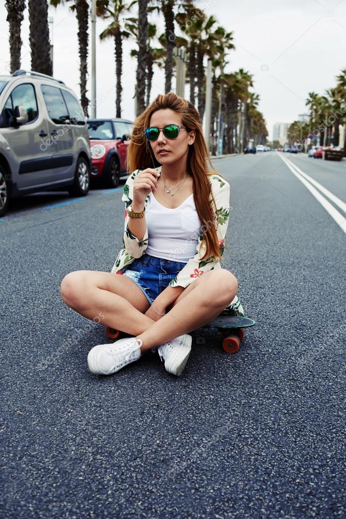hipster girl sitting  in the middle of asphalt road