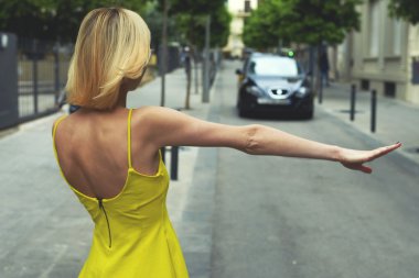woman in yellow dress hailing a taxi