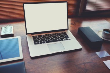 Laptop computer with white blank copy space screen for text message or publicity content lying on wooden table with digital tablet and stylish accessories