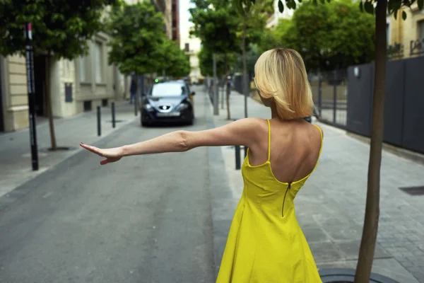 Woman in yellow dress hailing a cab taxi — Stock fotografie
