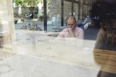 Worried and thoughtful businessman or entrepreneur sitting front open laptop computer in modern coffee shop interior in urban setting