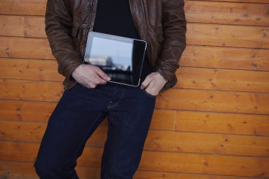 Hipster student with touch pad standing on wooden background
