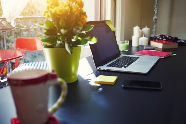 On the table in the office is a laptop next to a bright yellow flowers in a pot