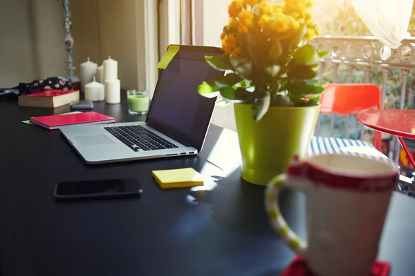Auf dem Tisch im Büro steht ein Laptop neben einer leuchtend gelben Blume im Topf — Stockfoto