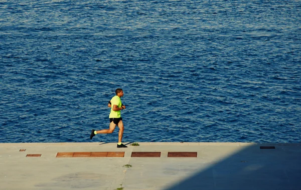 Deportista corriendo sobre la carretera cerca del mar —  Fotos de Stock