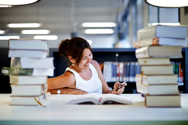 Ung dam med smartphone i ett bibliotek — Stockfoto