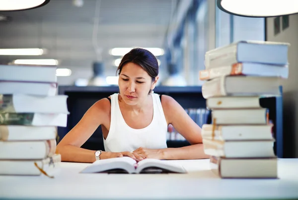 Kvinnlig student som läser en bok i ett bibliotek — Stockfoto