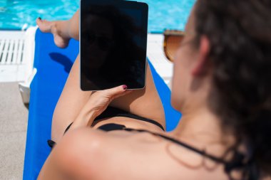 Woman using tablet while sunbathing near pool