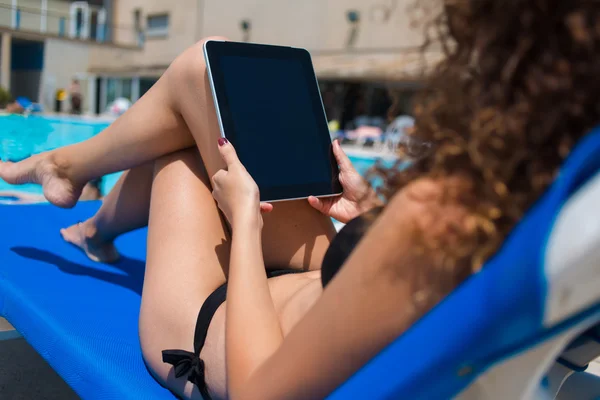 Femme utilisant la tablette tout en bronzant près de la piscine — Photo