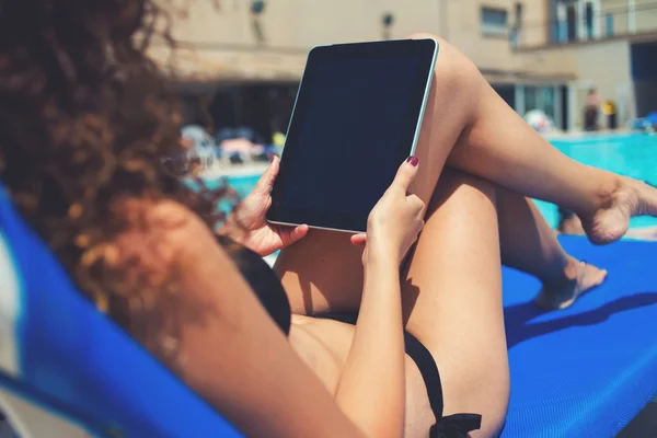 Mujer usando tableta mientras toma el sol cerca de la piscina — Foto de Stock