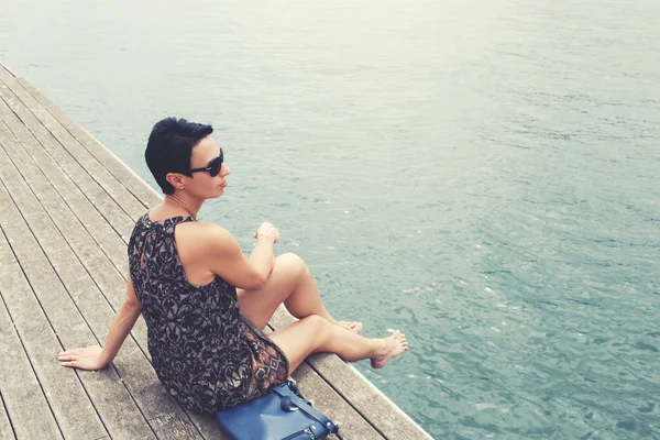 Woman sitting on the wooden pier near sea — ストック写真