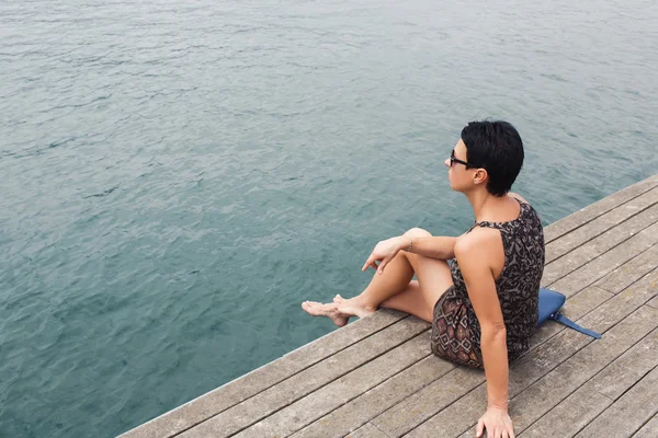 Charming woman sitting on a wooden pier — Stock fotografie