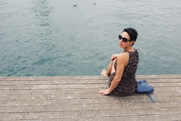 Woman sitting on the wooden pier near sea — Stock fotografie