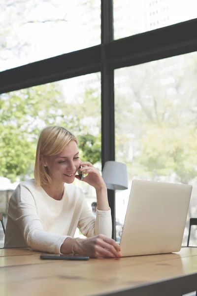 Woman working on net-book and talks on smartphone — Stock Photo, Image