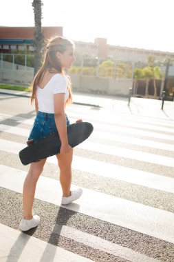 Woman with longboard crosses the road